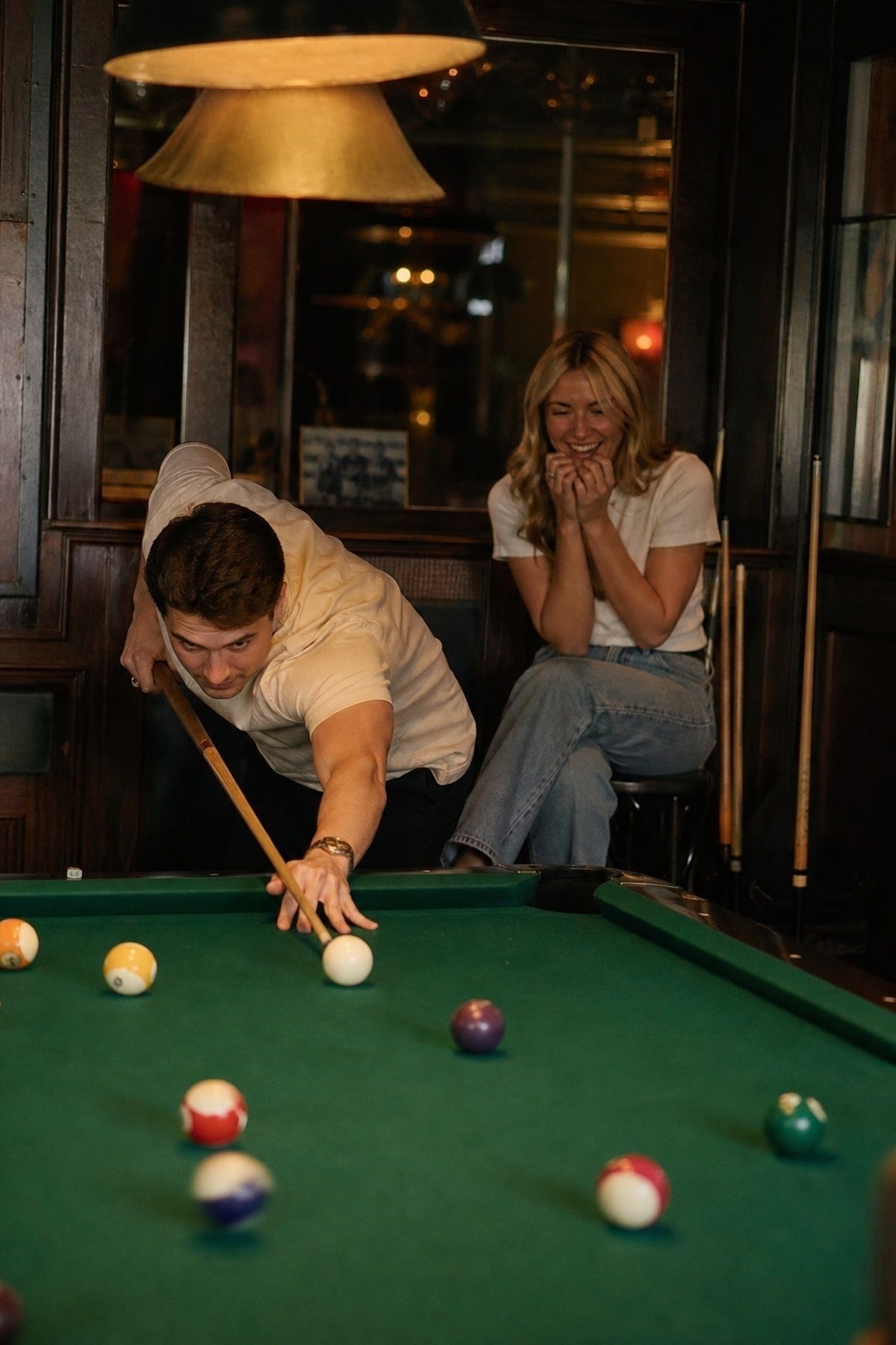 Pool table engagement break shot with one partner reacting from a nearby stool