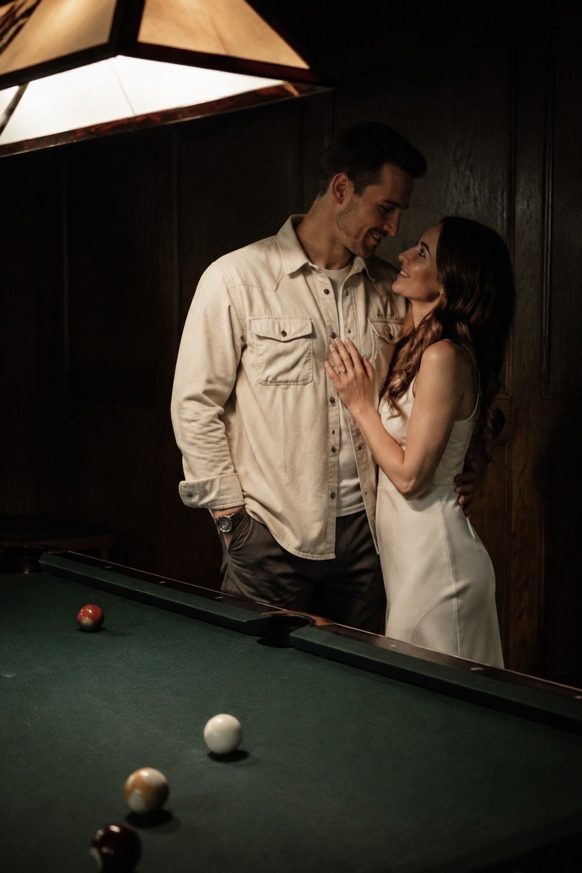 Pool table engagement couple under warm overhead billiards lighting with clear faces