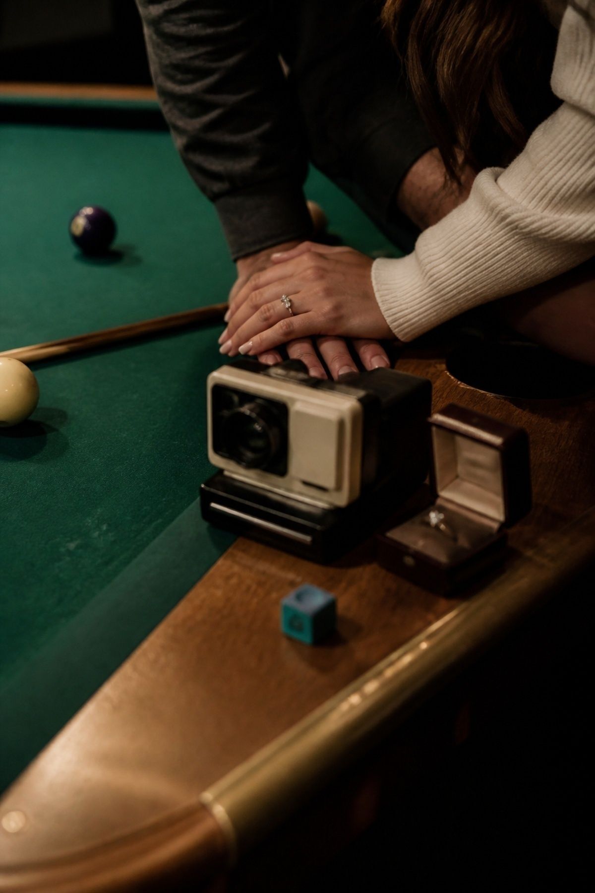 Pool table engagement personal detail with an instant camera and ring box near cue chalk