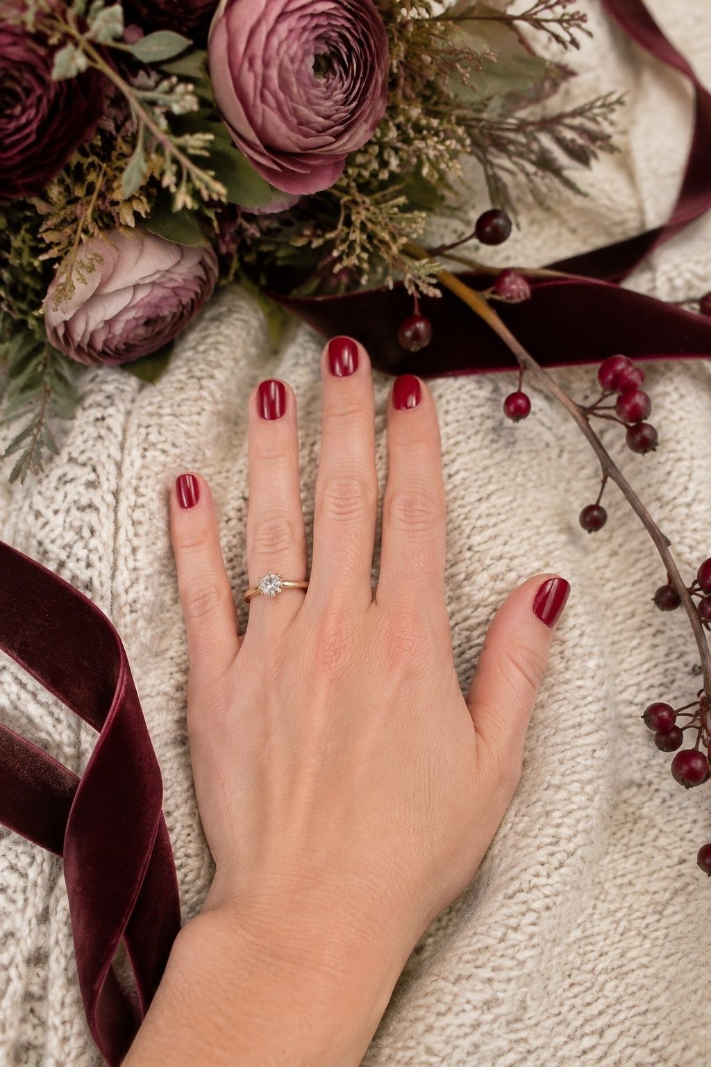 Cranberry bridal nails with mauve flowers, berries, velvet ribbon, and a cream knit wrap.
