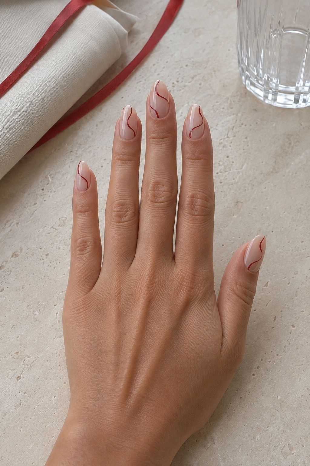 Sheer bridal nails with fine negative-space red swirls on pale stone.