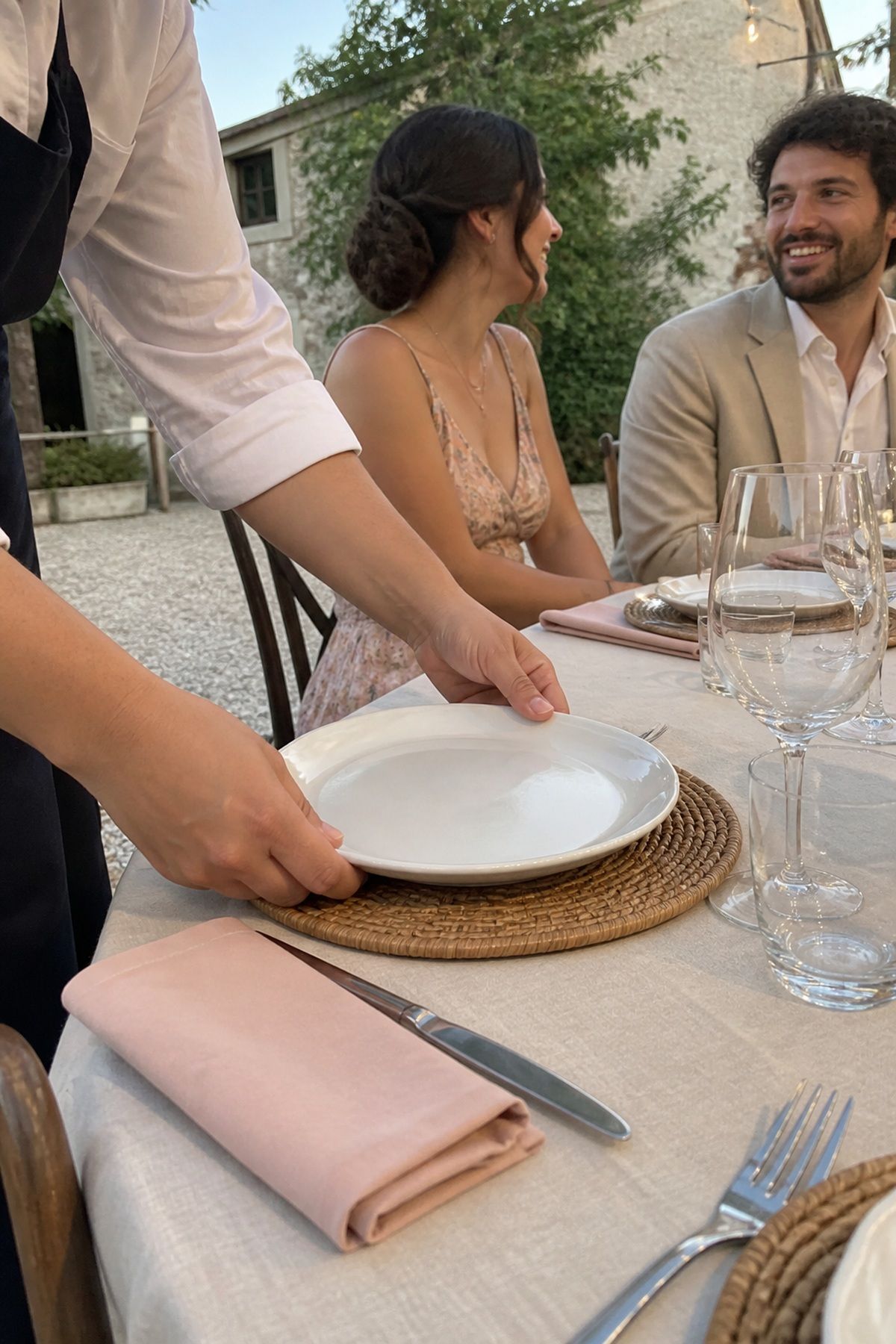 A server sets a simple white plate on a woven rattan charger.