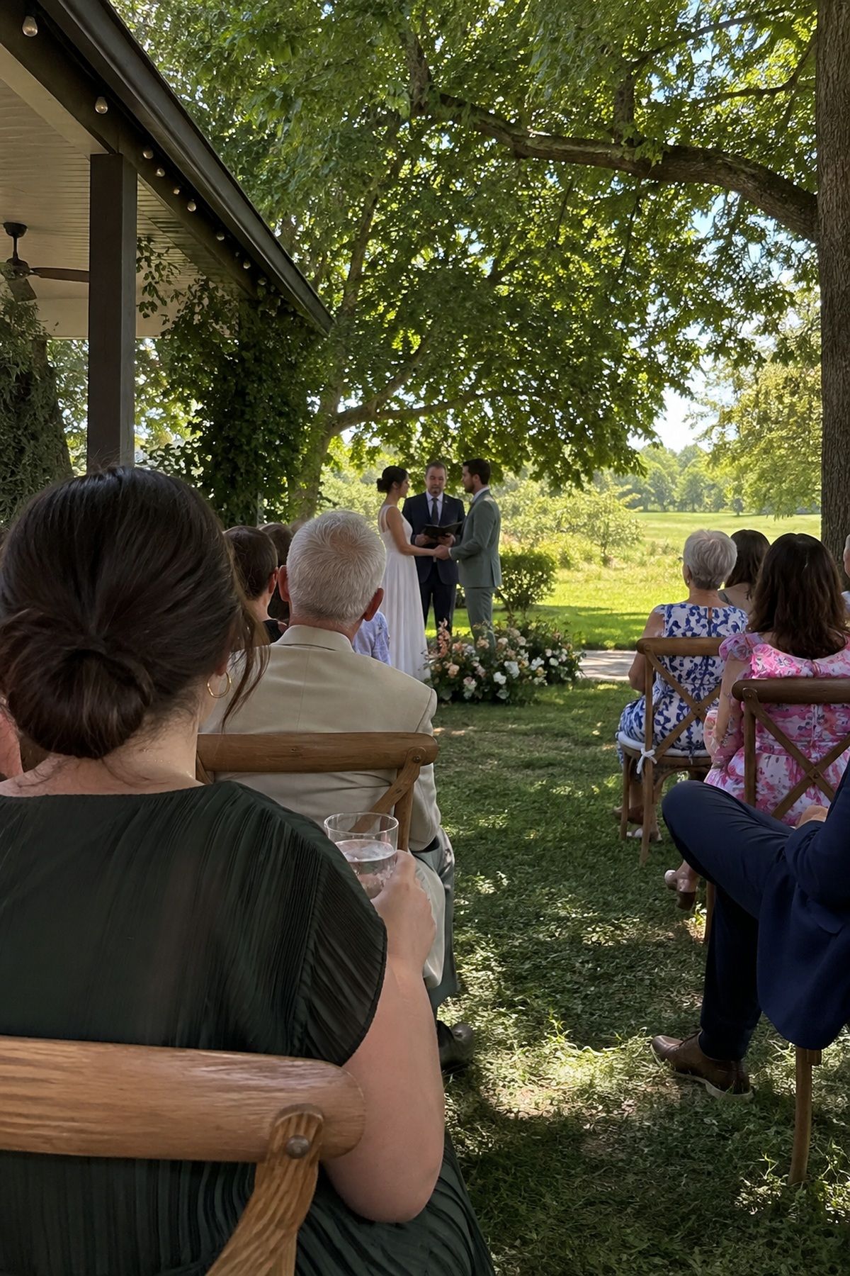 Guests attend a summer garden ceremony arranged around deep natural shade.