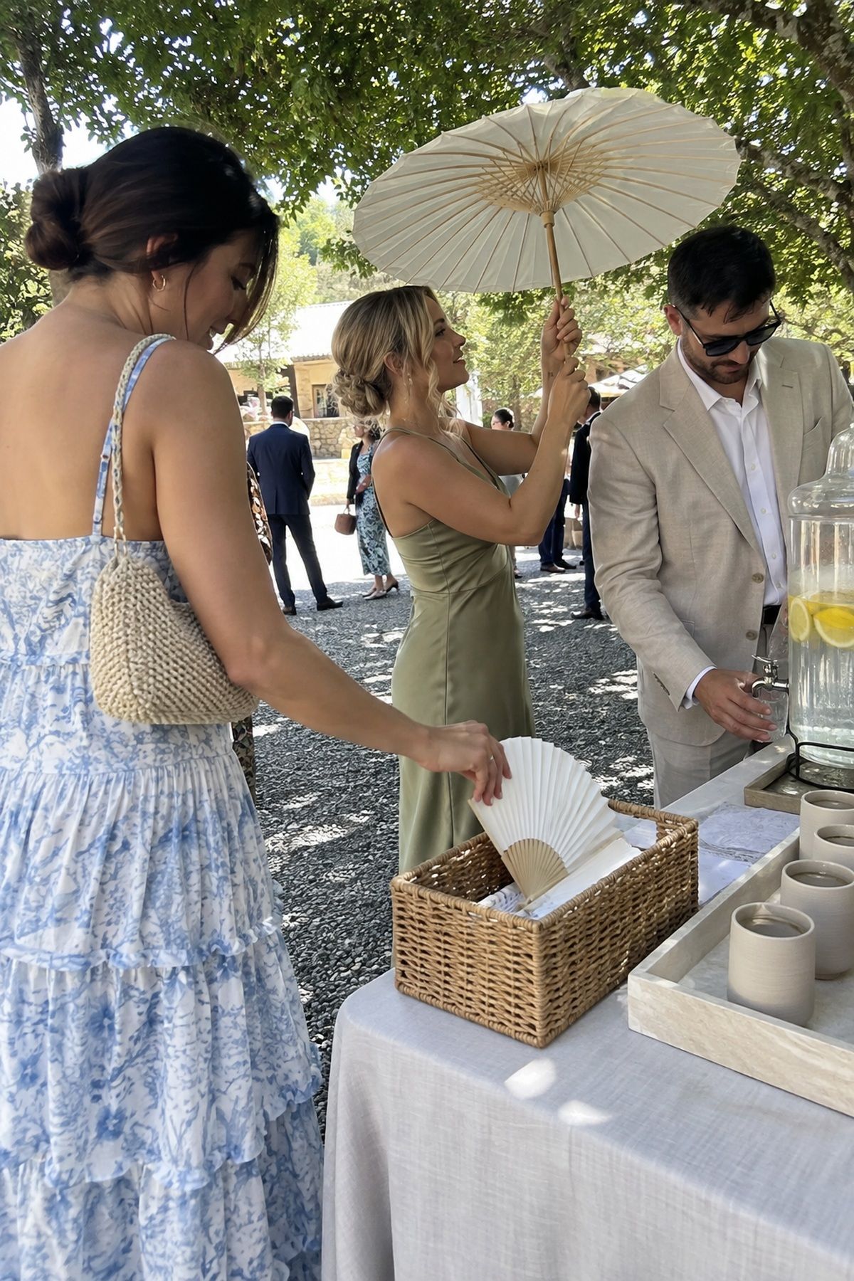 Guests use coordinated fans, a parasol, and lemon water at a shaded arrival station.
