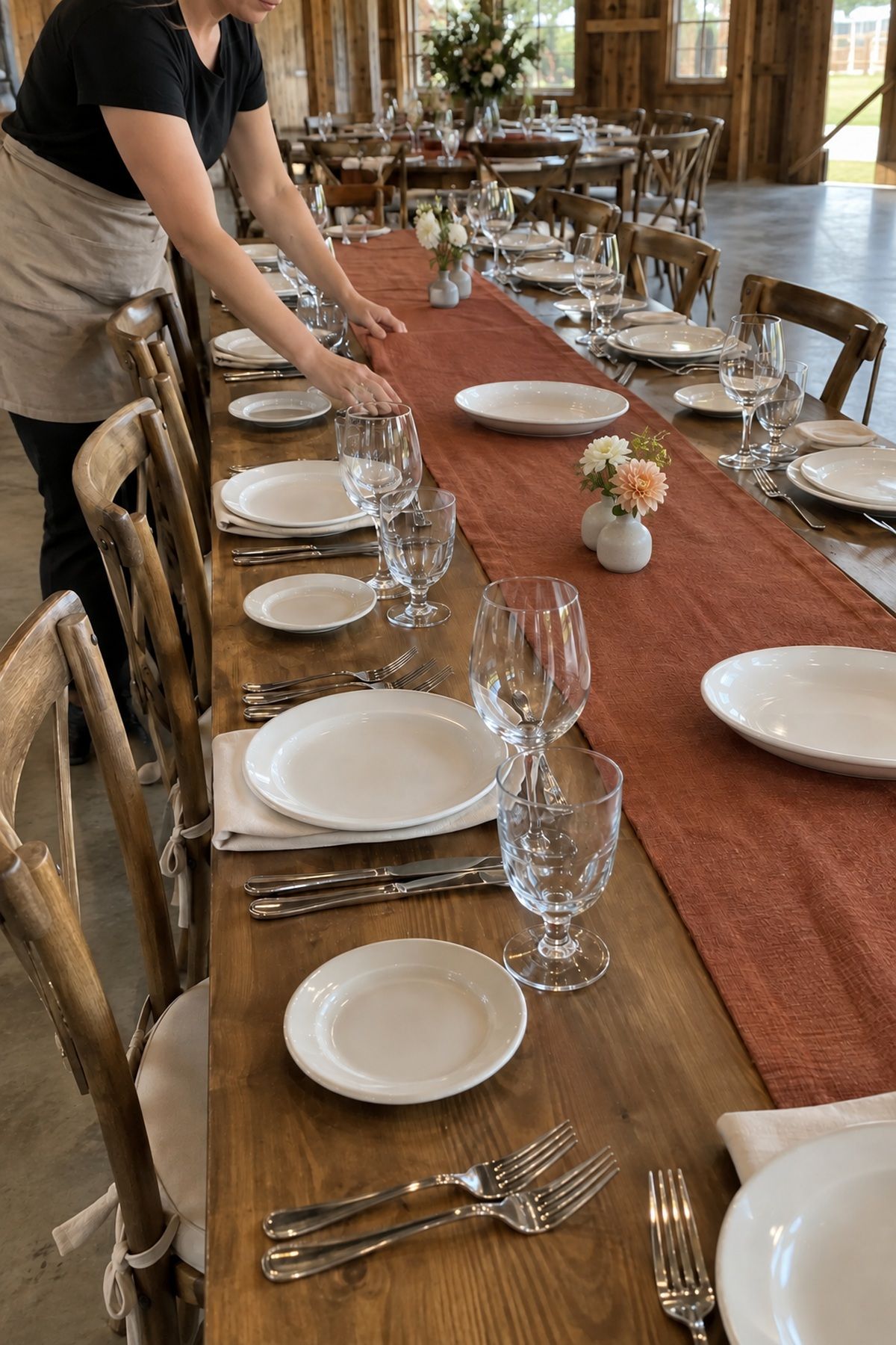 A flat rust linen runner and low flowers leave full place settings and platter spaces clear.