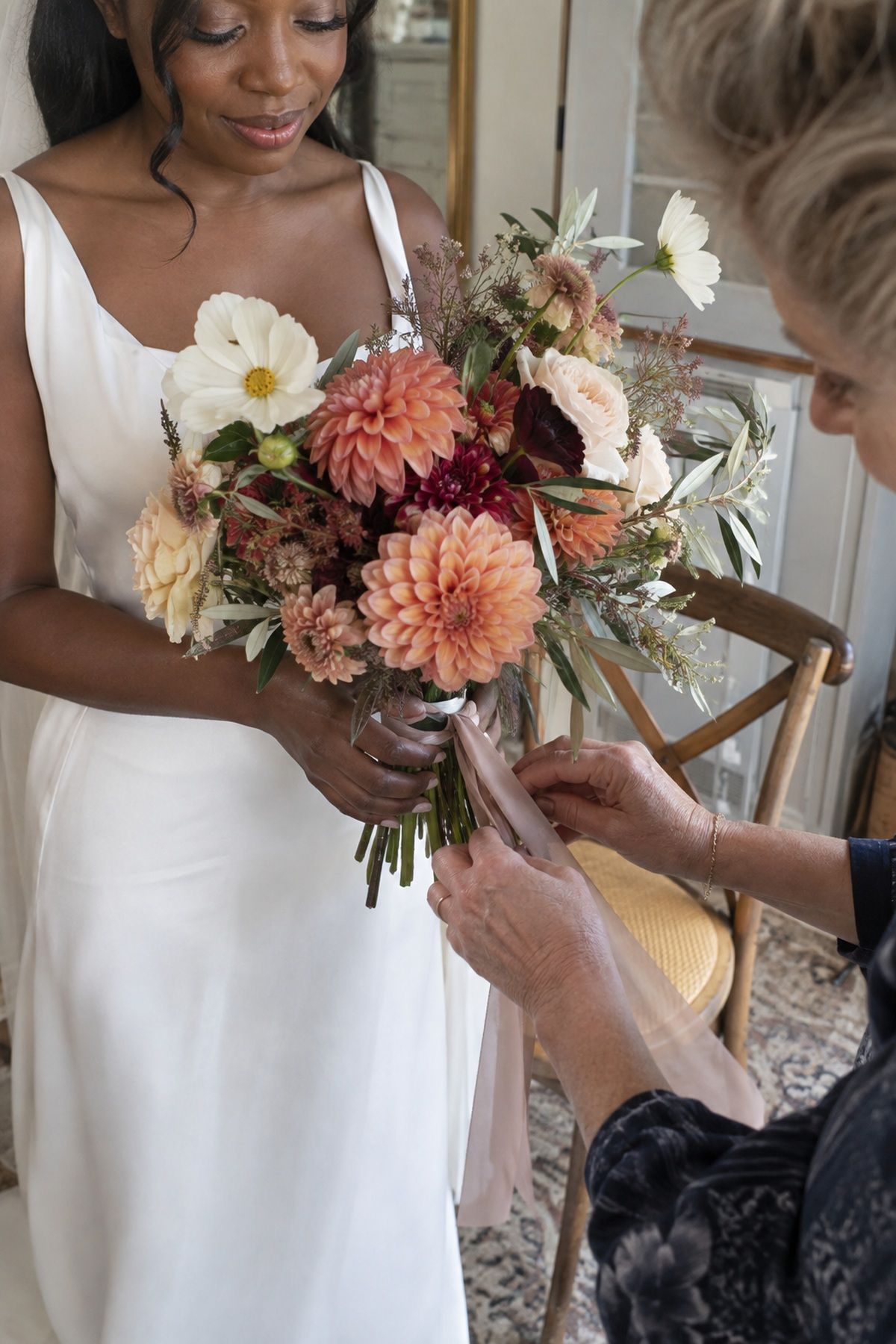 A florist finishes a peach dahlia bouquet in a September wedding getting-ready room.