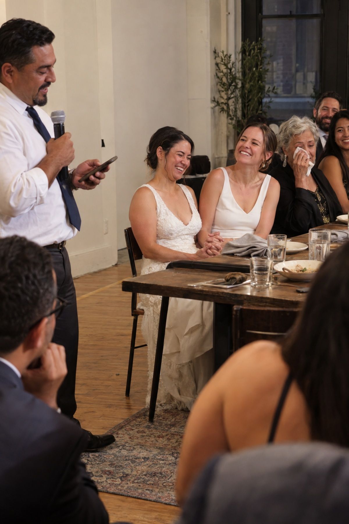 Two brides and their family react warmly to a wedding toast.