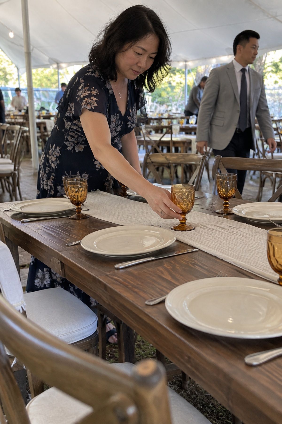 A guest straightens amber glassware beside ivory wedding plates.