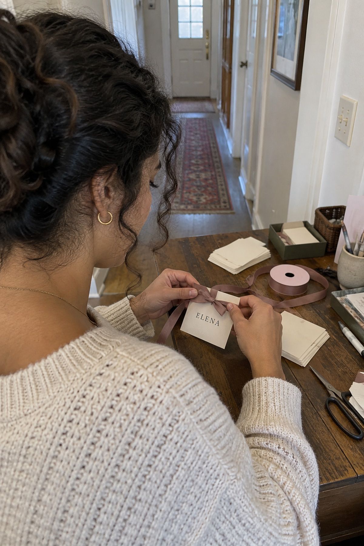 A wedding guest ties mauve ribbon around a custom place card for Elena.