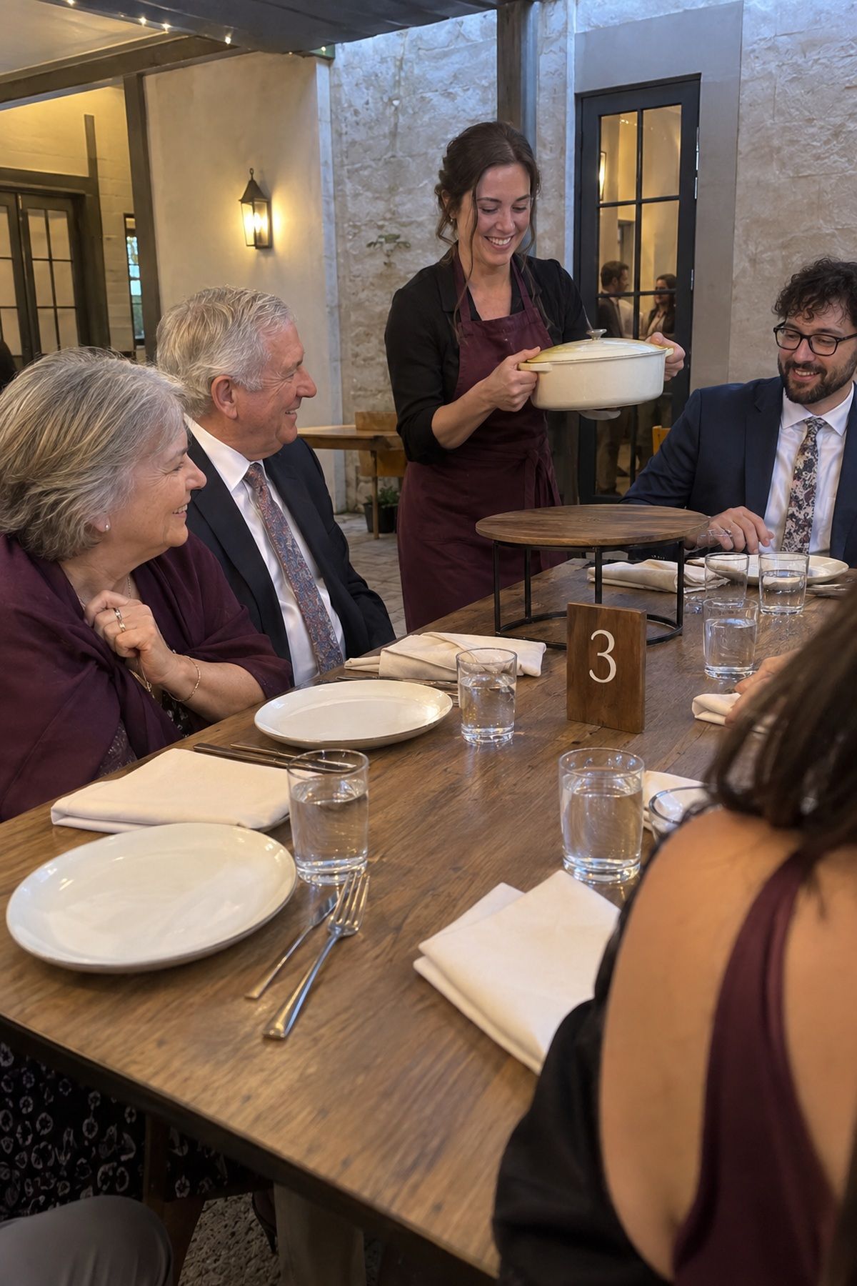 A host brings dinner to guests gathered around a simple early-harvest wedding table.