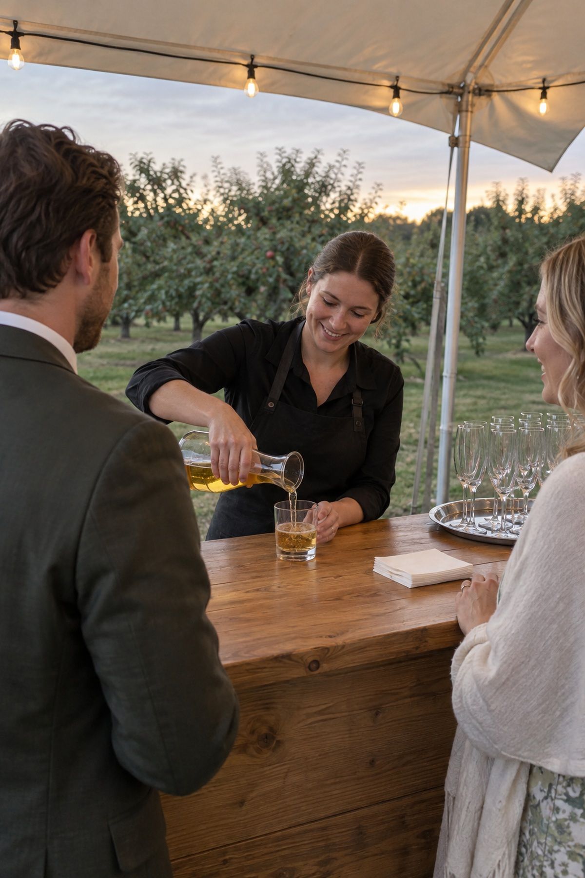 A bartender pours cider for guests at a simple September orchard cocktail hour.
