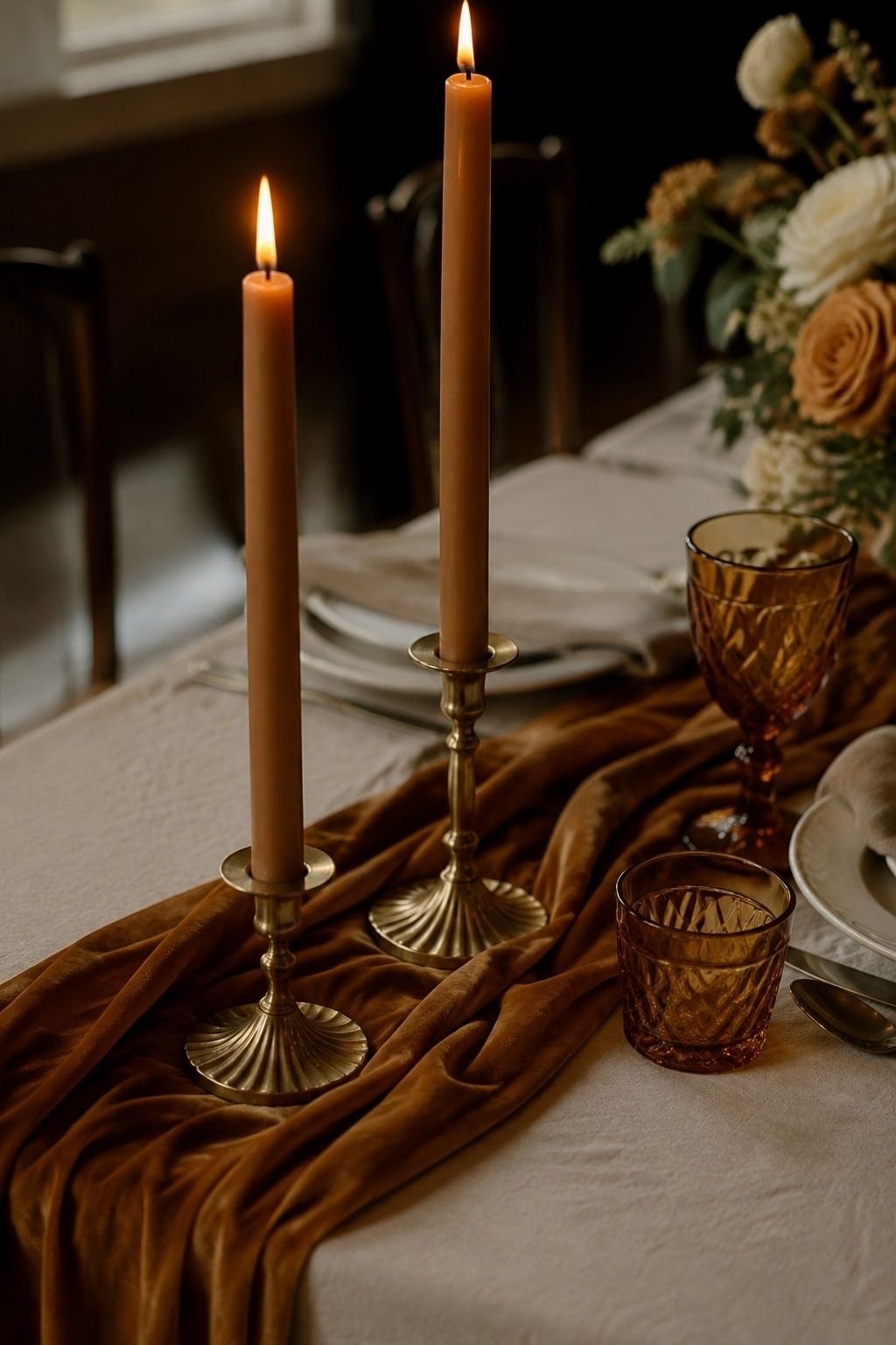 Caramel taper candles and amber goblets warm an ivory wedding table.