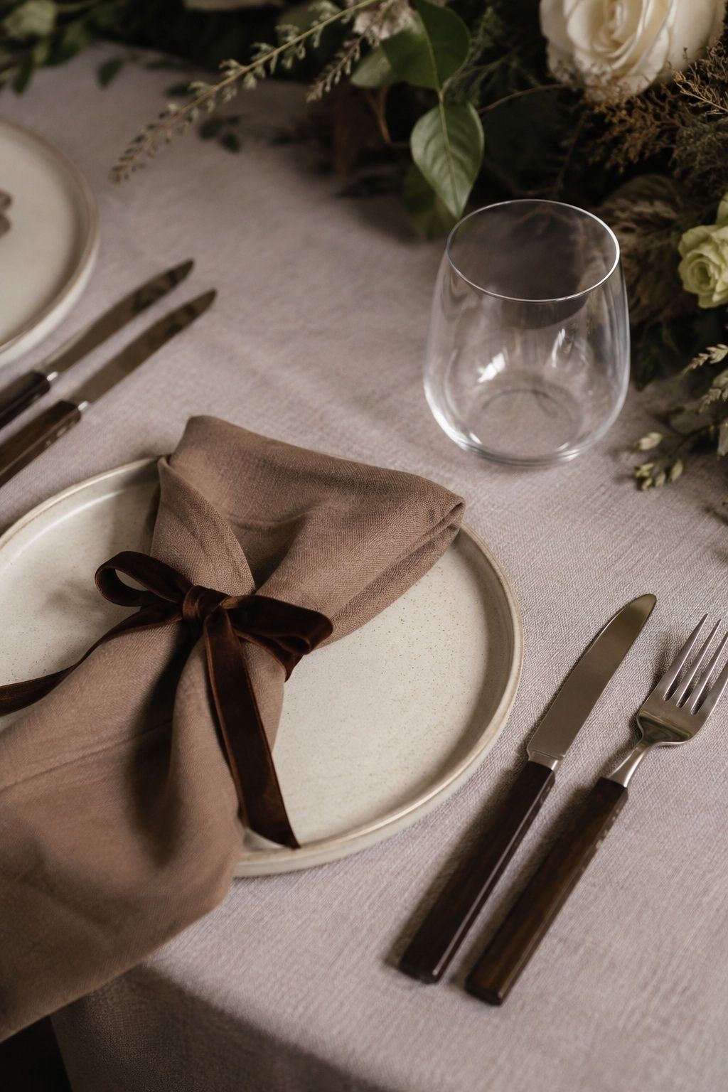 Espresso flatware handles and velvet ribbon contrast with pale taupe linen.