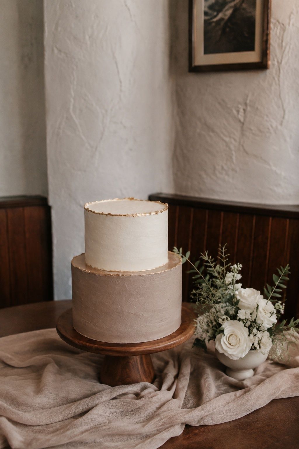 Mocha and cream wedding cake with gold edging on a walnut-toned stand.