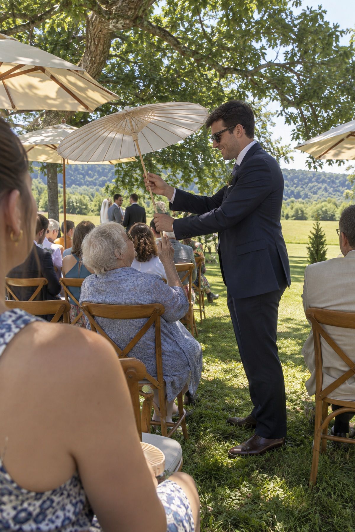 An usher offers an older wedding guest a parasol beneath shaded summer ceremony seating.