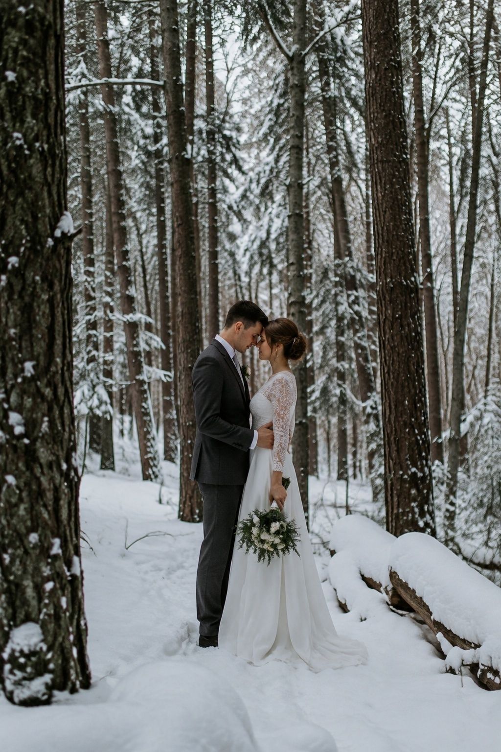Newlywed couple posing between tall snow covered trees