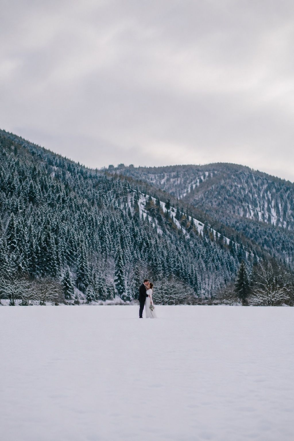 Tiny newlywed couple centered in a wide snowy mountain landscape