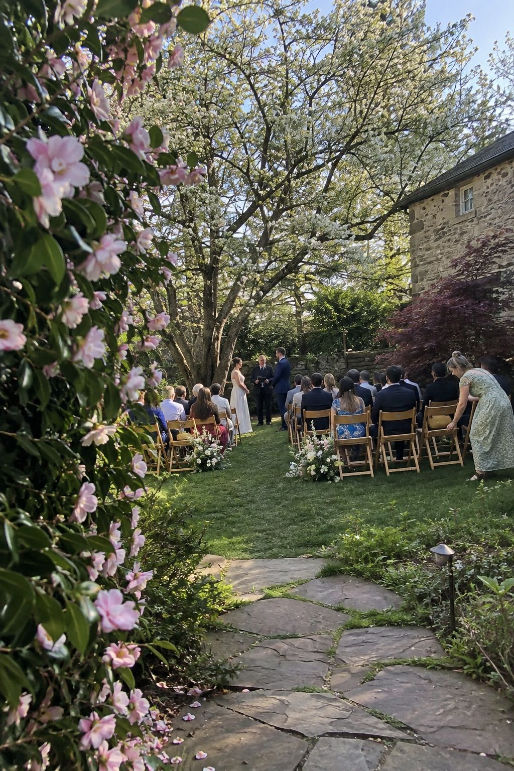 Intimate spring wedding ceremony framed by flowering garden trees and a stone path
