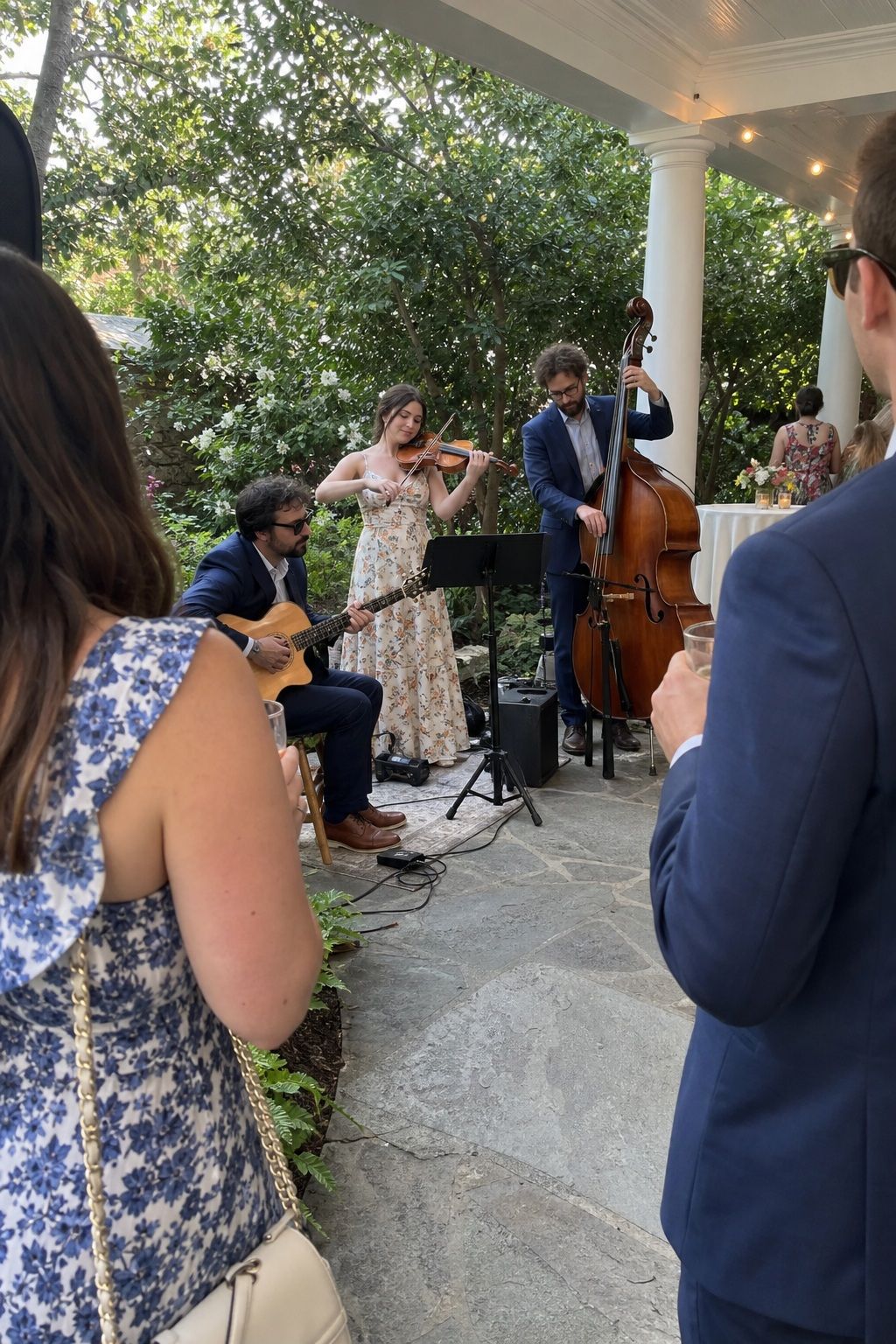 Acoustic wedding trio playing guitar, violin, and upright bass under a veranda