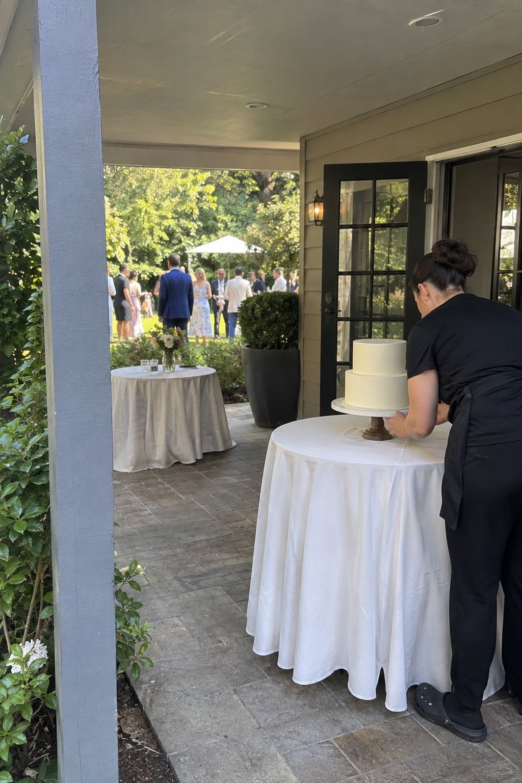 Caterer checking a simple wedding cake on a shaded veranda near the service door