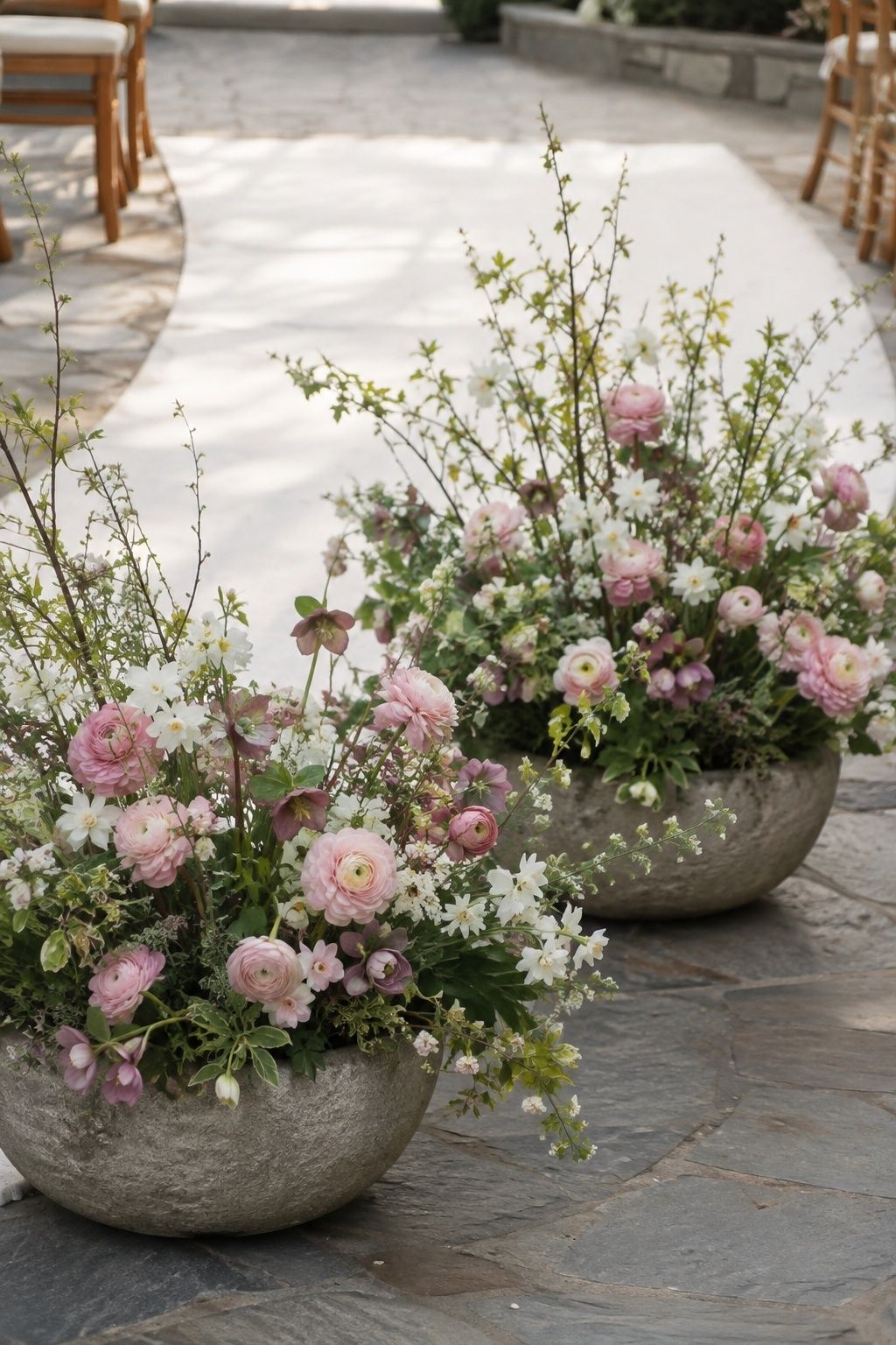 Low stone bowls of pink and white spring flowers beside an open ceremony aisle