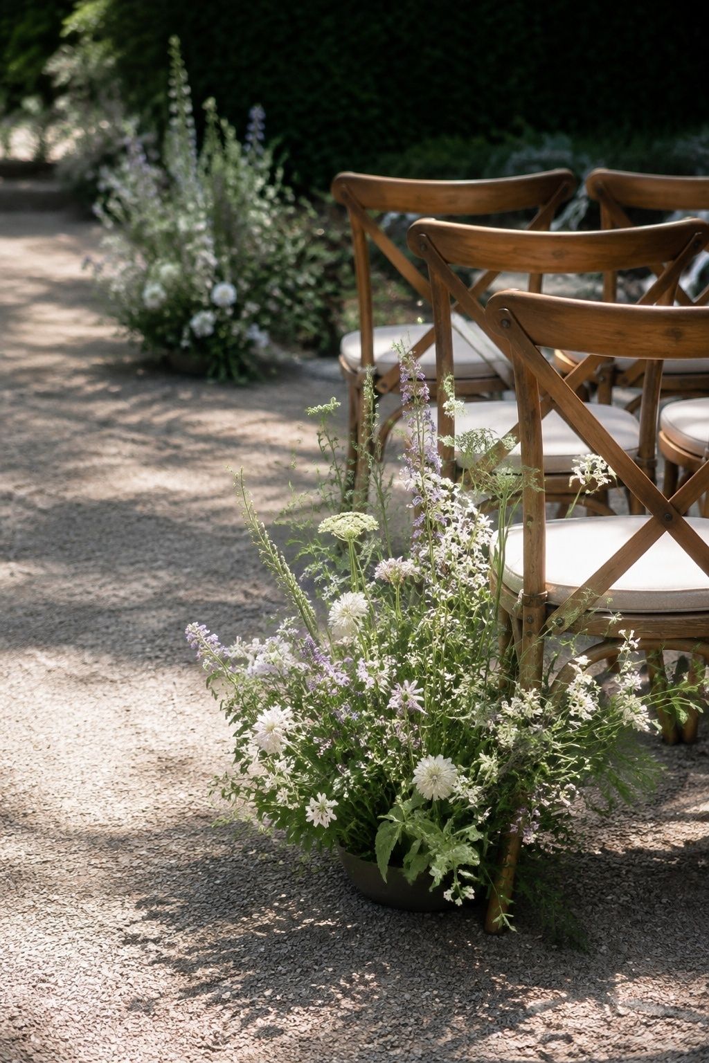 Low lateral view of meadowy white and lavender spring ground-flower clusters in discreet weighted low vessels beside row ends in a garden ceremony