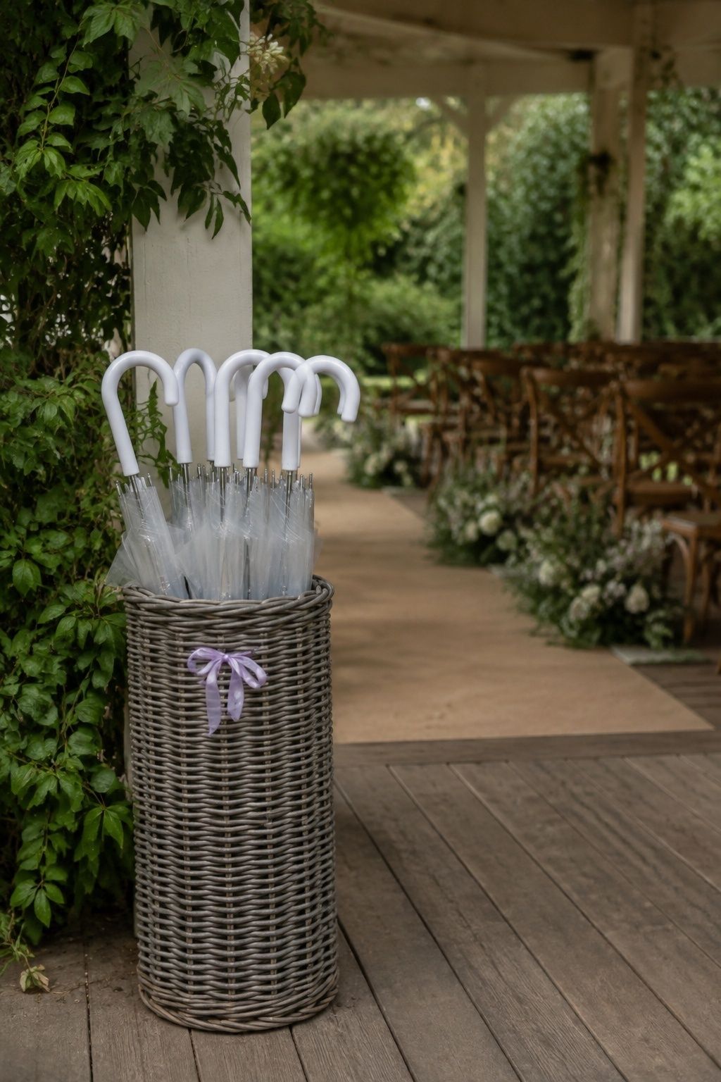 Medium view of tall sturdy woven umbrella basket holding six closed transparent umbrellas with clean white curved handles