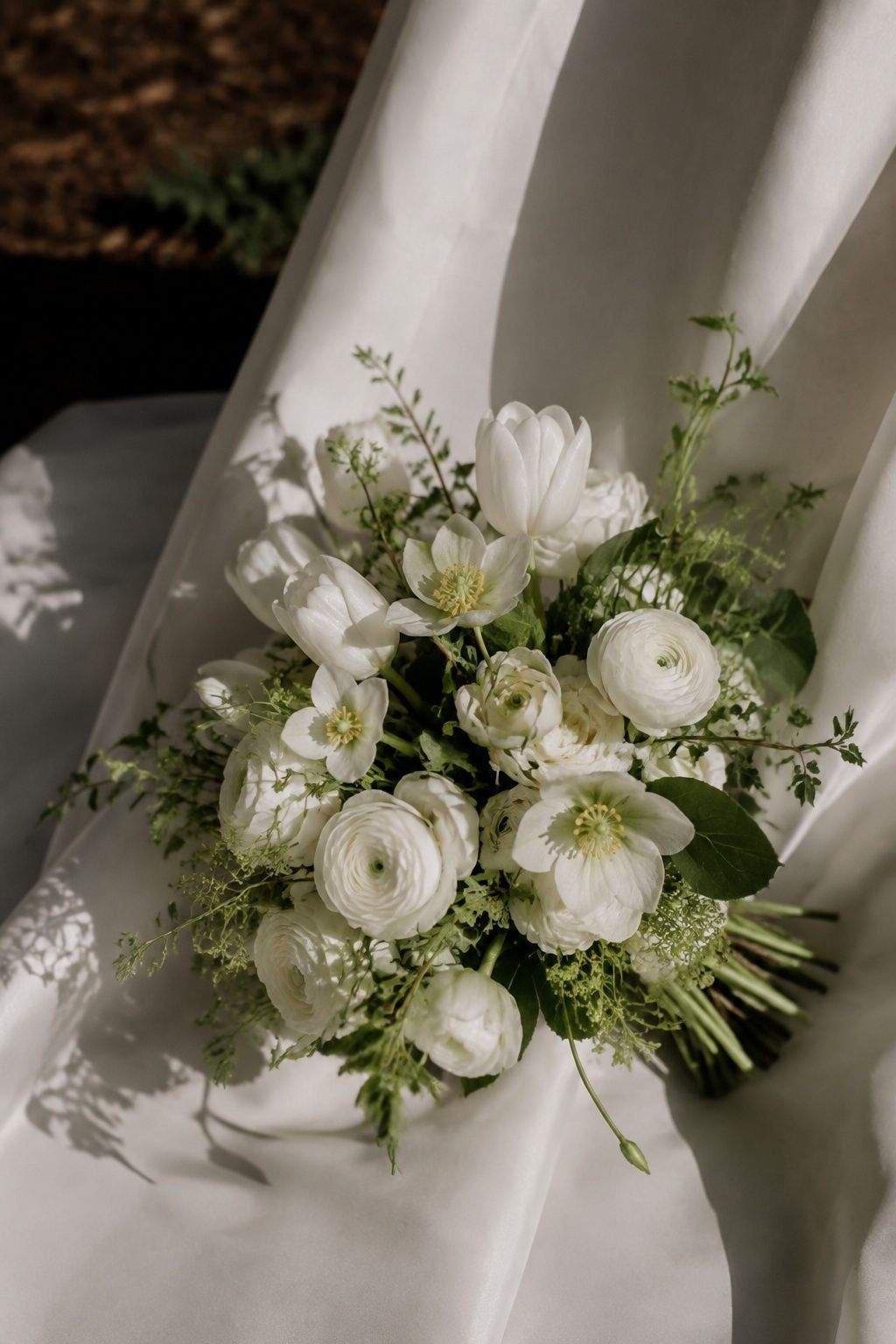 White tulips and ranunculus with green-centered hellebores against white satin
