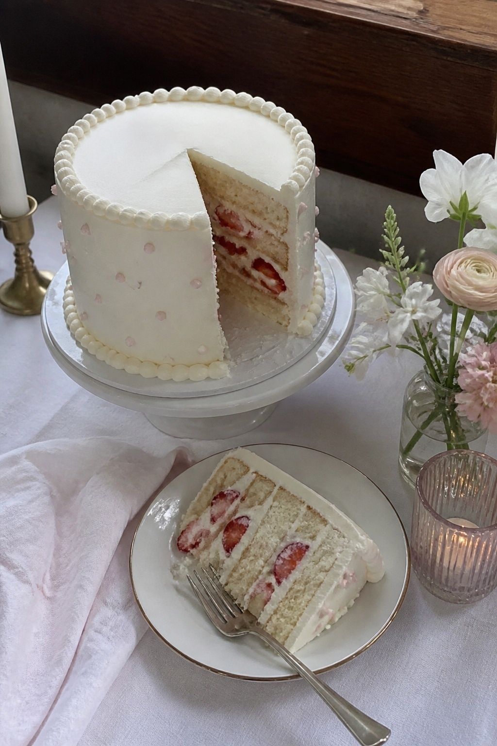 Slightly overhead view of a vanilla strawberry layer cake with one slice on a plate exposing ripe strawberry filling.