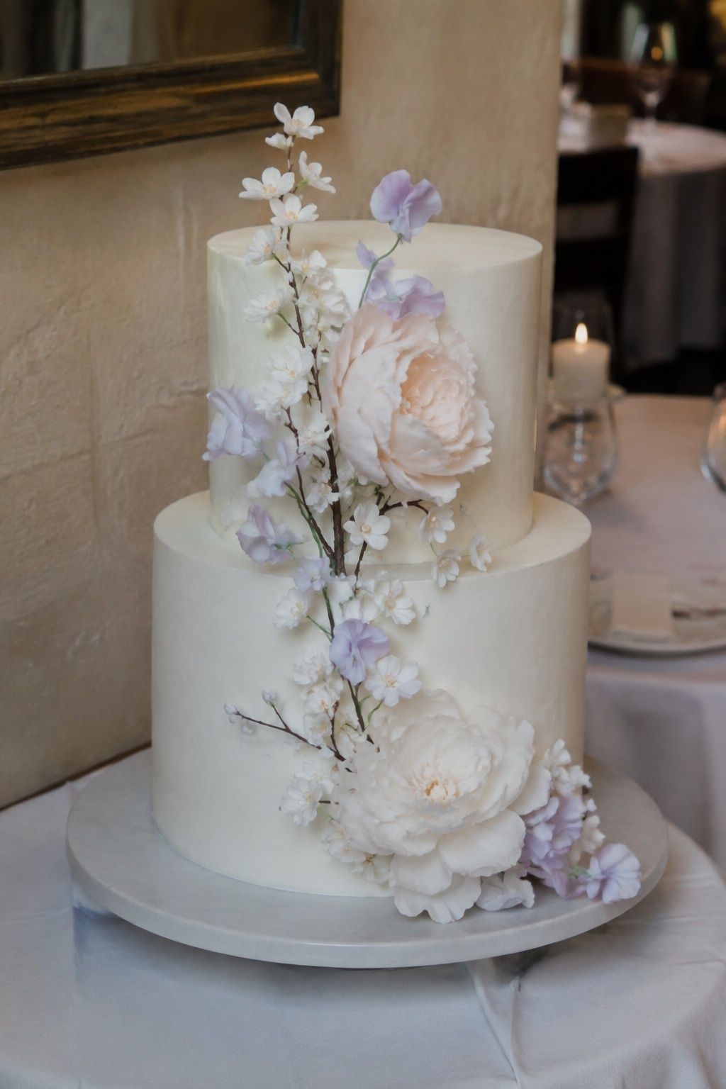Low three-quarter portrait of a compact two-tier ivory cake with delicate handcrafted sugar peonies.