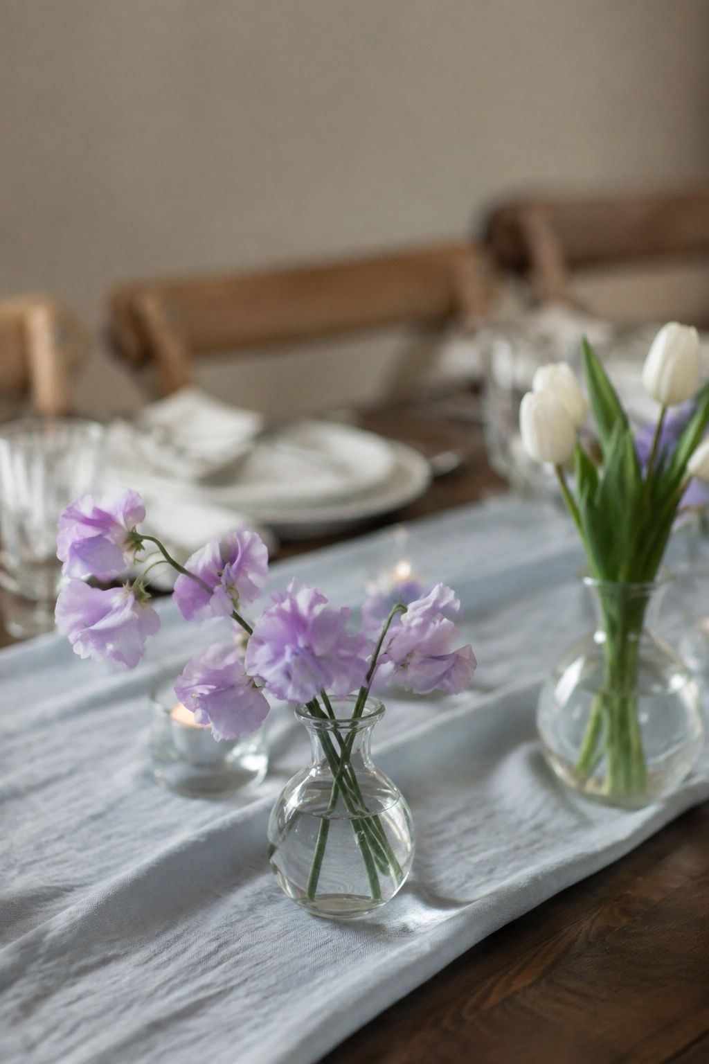 Intimate side-angle detail of a tiny transparent vase containing four lavender sweet pea stems with fluttering petals