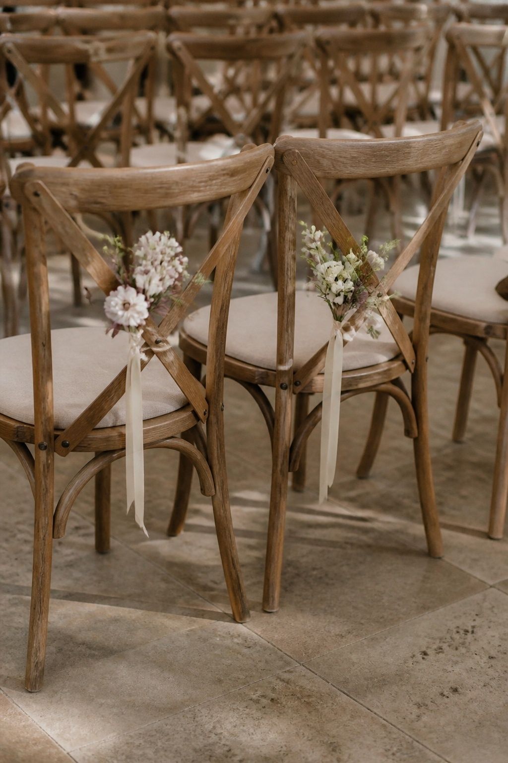 Close three-quarter view of two aisle-side front row wooden chairs with small tied spring posies and short ivory ribbons