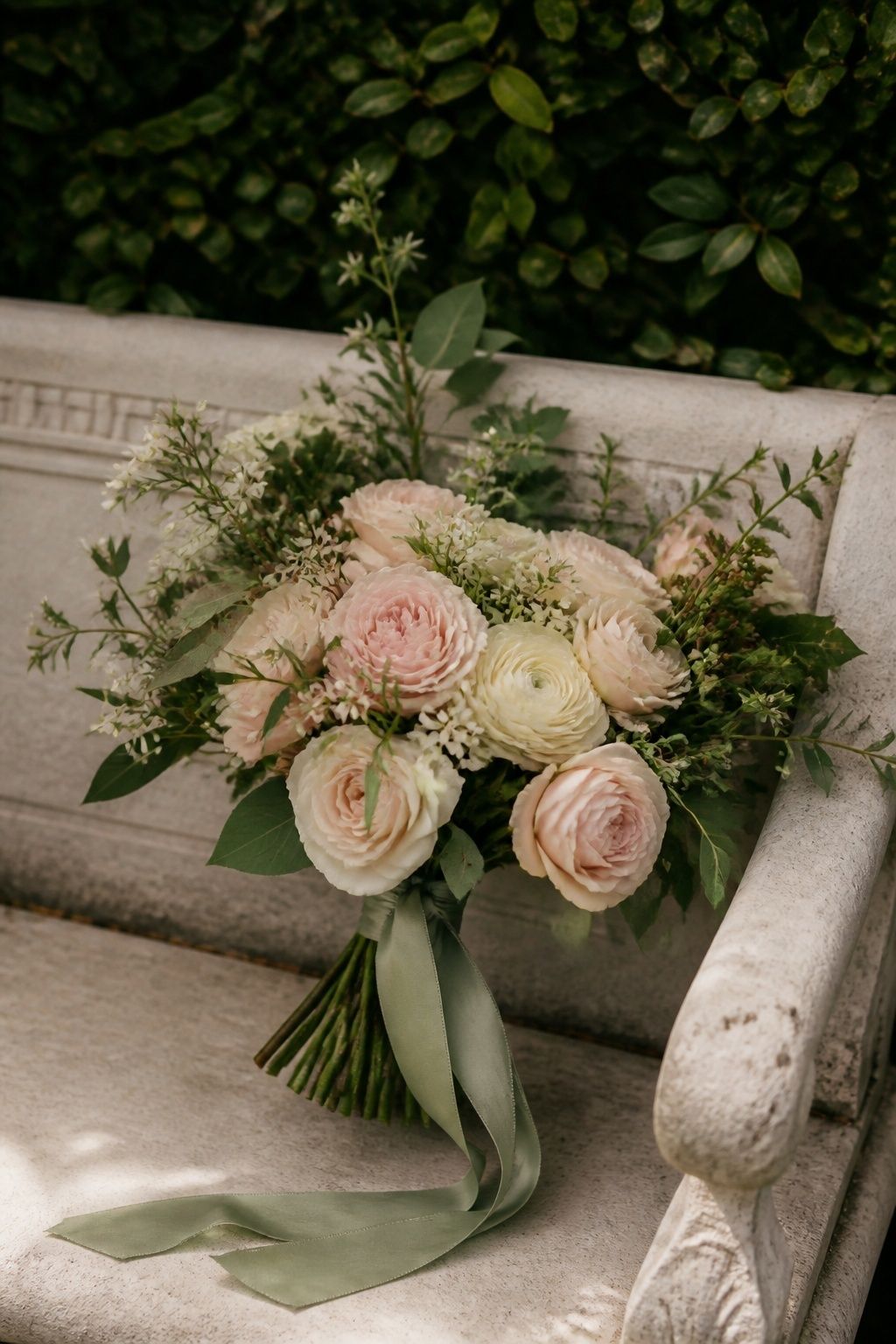Blush and cream bridal bouquet with sage ribbon on a garden bench