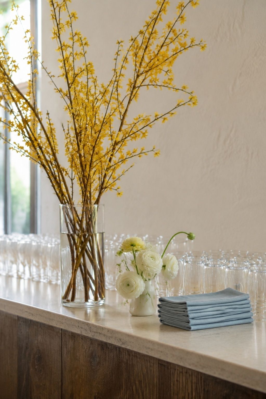 Yellow forsythia branches beside white flowers and blue napkins at a wedding bar.