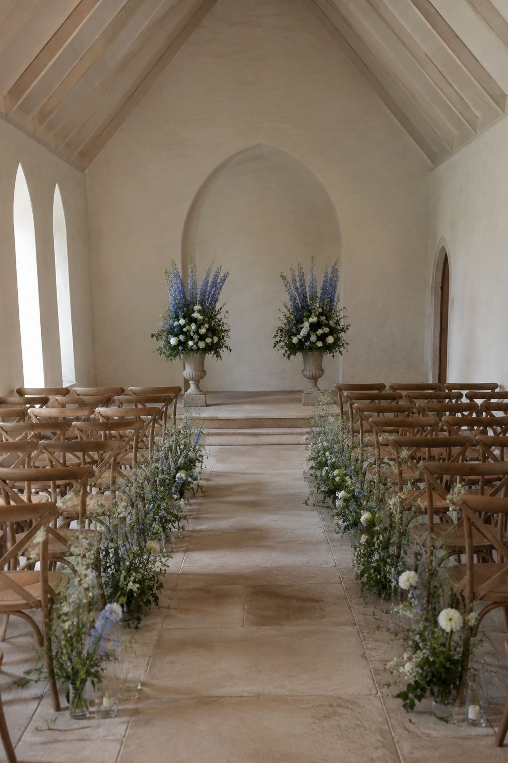 Blue delphinium aisle arrangements and altar urns in a small chapel.