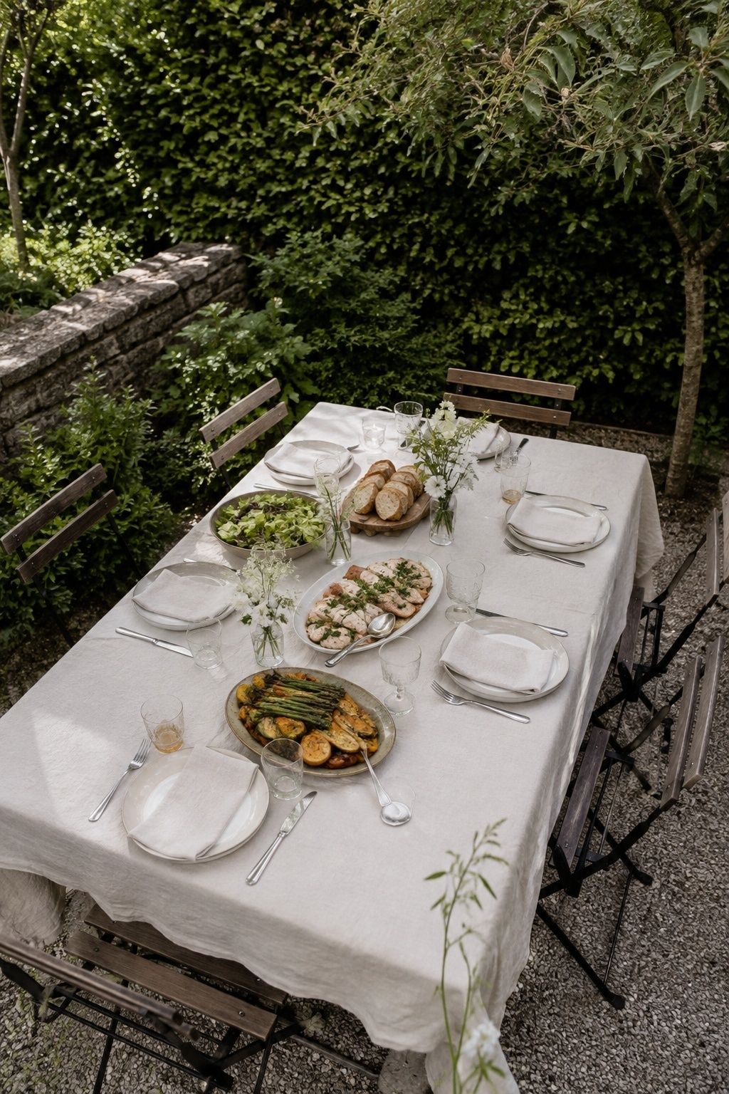 A small rectangular garden wedding table set for six with shared platters of herb chicken and spring vegetables