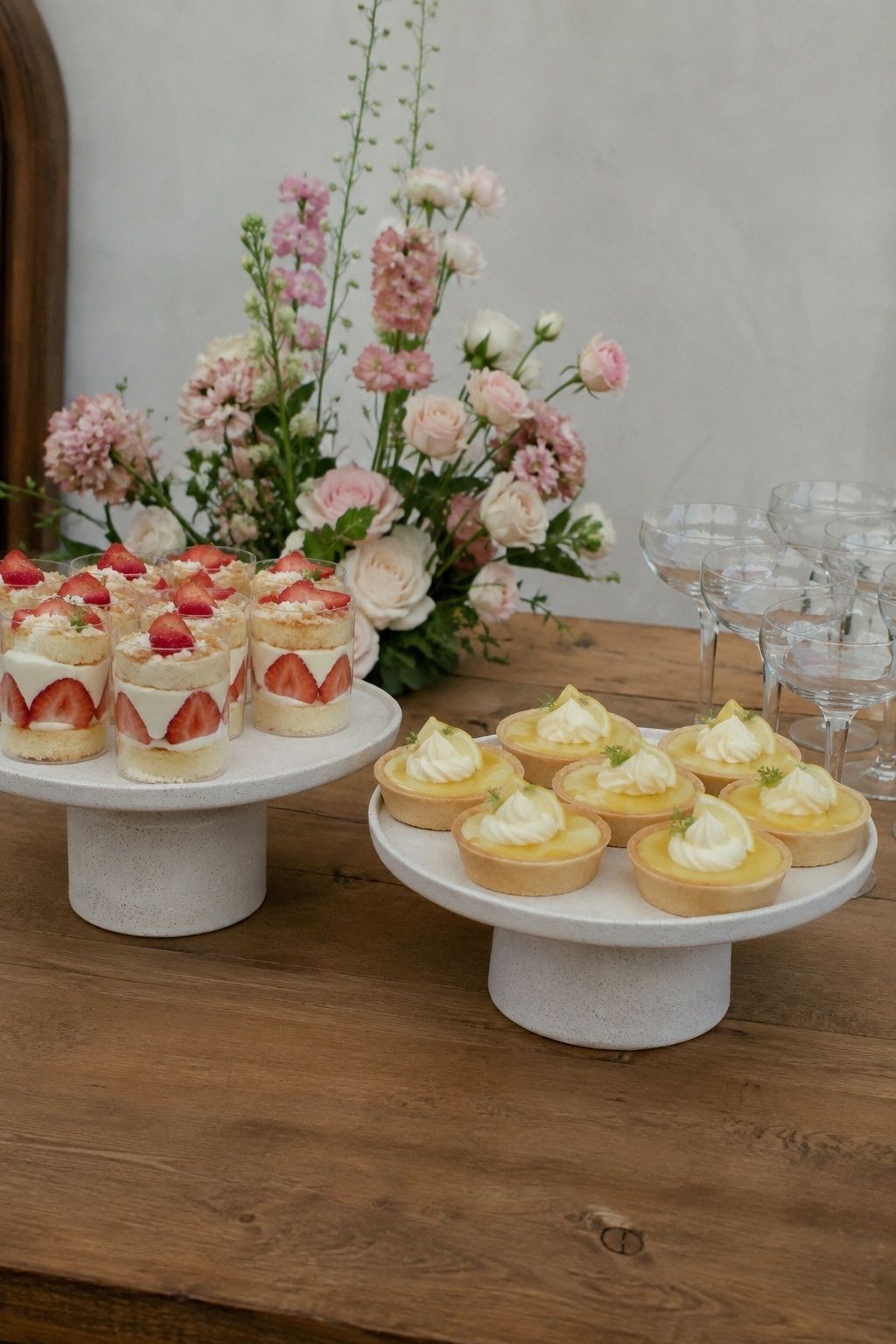 Small wedding dessert display with mini lemon tarts and individual strawberry shortcake cups on two low ceramic stands