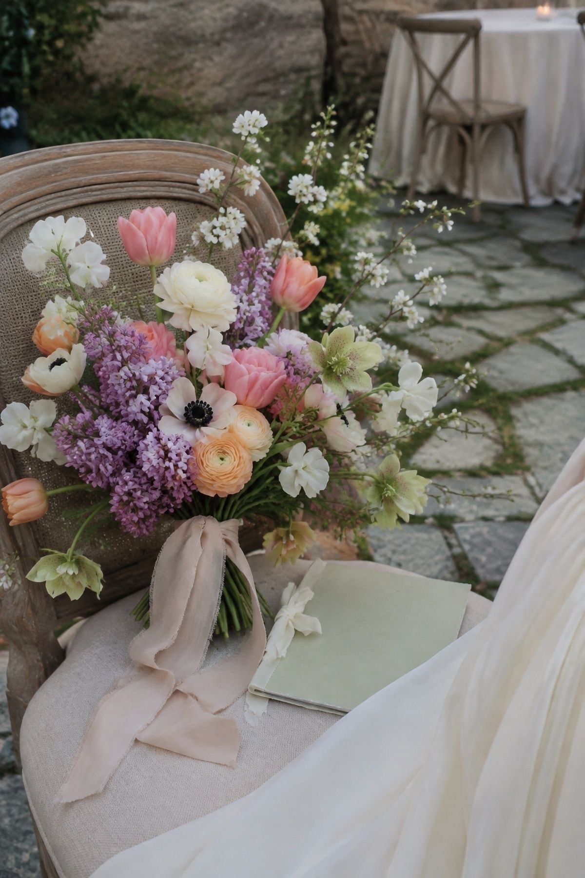 Spring wedding bouquet detail with tulips, ranunculus, sweet peas, lilacs, hellebores, anemones, flowering branches, ribbon, and vow book
