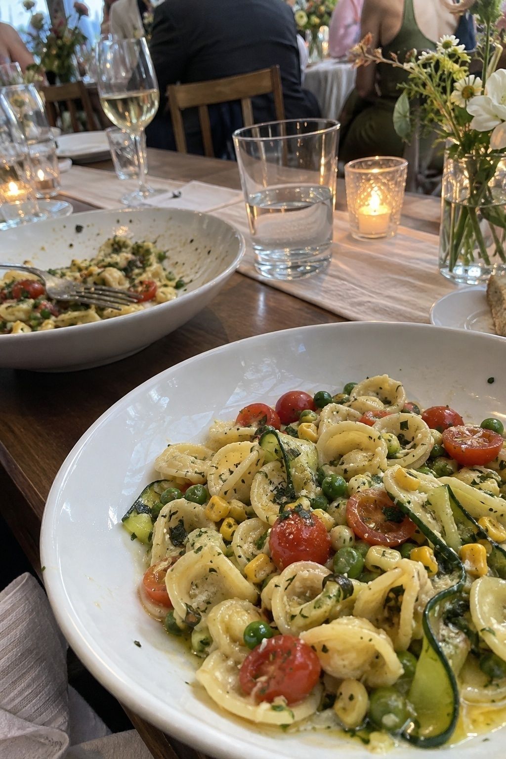Light lemon herb summer pasta with tomatoes zucchini corn and peas at a wedding dinner