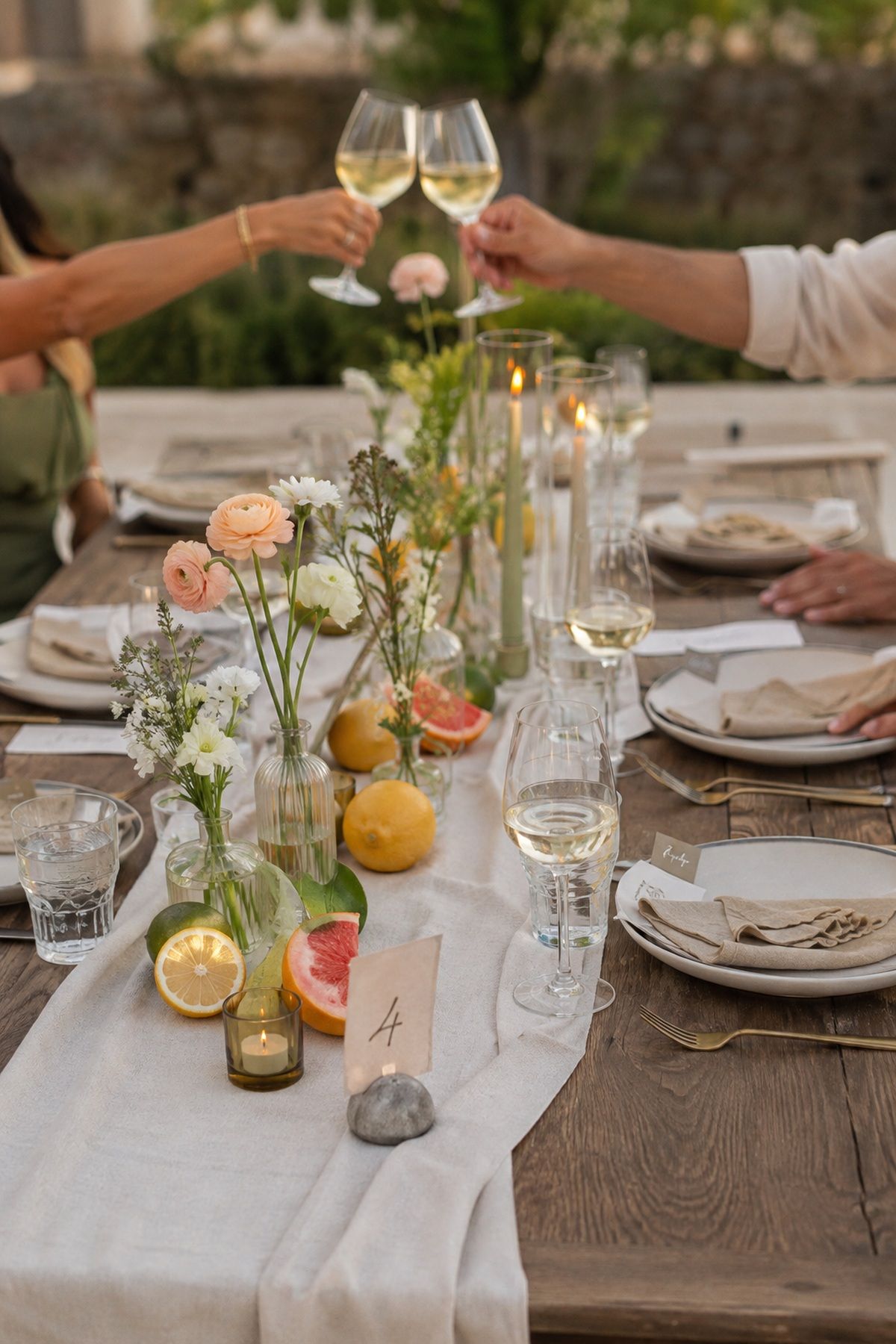 Summer wedding tablescape with linen runner, citrus accents, low flowers, candles, and guests toasting