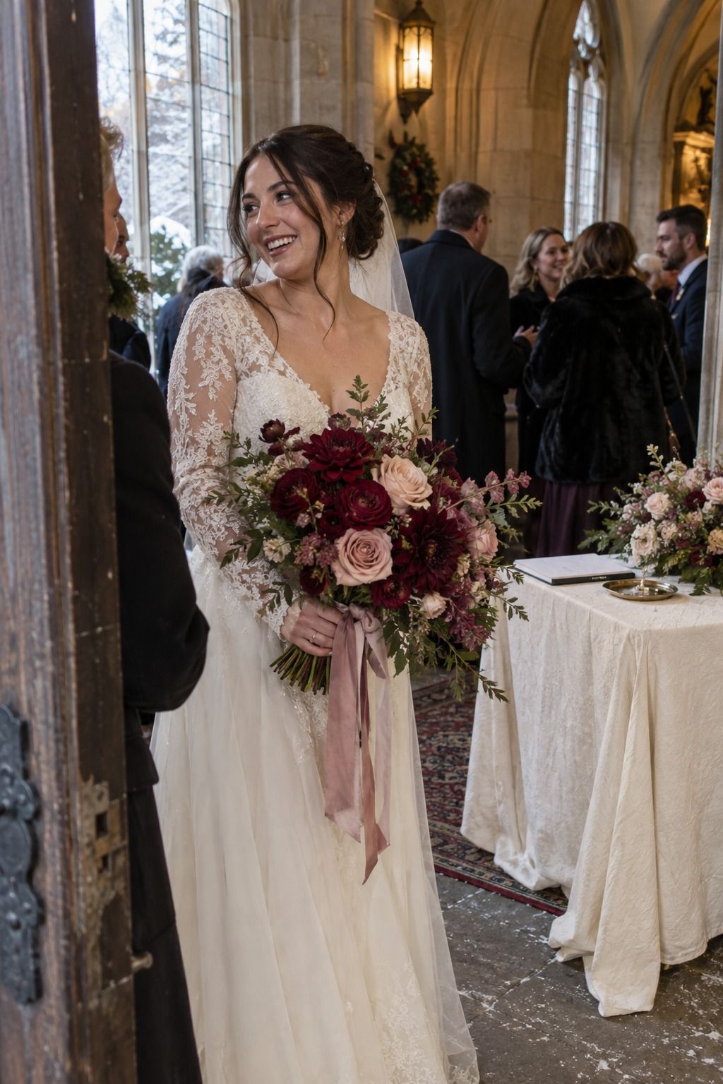 Valentines day wedding color palette in a candid small wedding moment: bride carries an oxblood and antique-rose bouquet with blush ribbon beside warm-ivory chapel details.