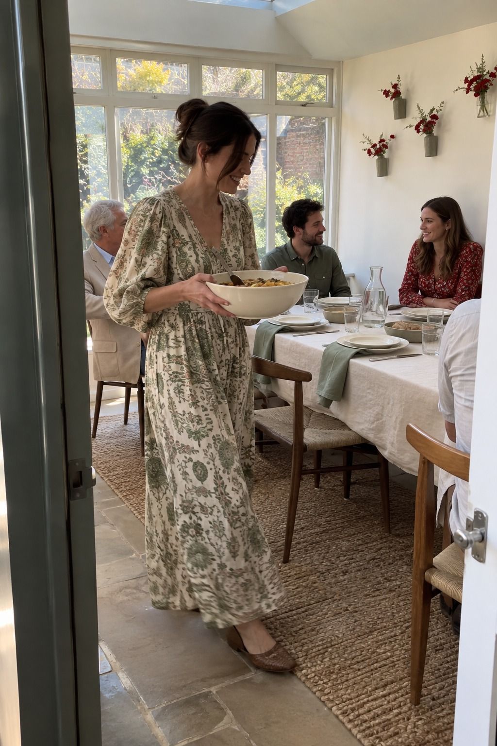 Guest carries a serving bowl through a home wedding dining room with cream linen, sage napkins and red accents.