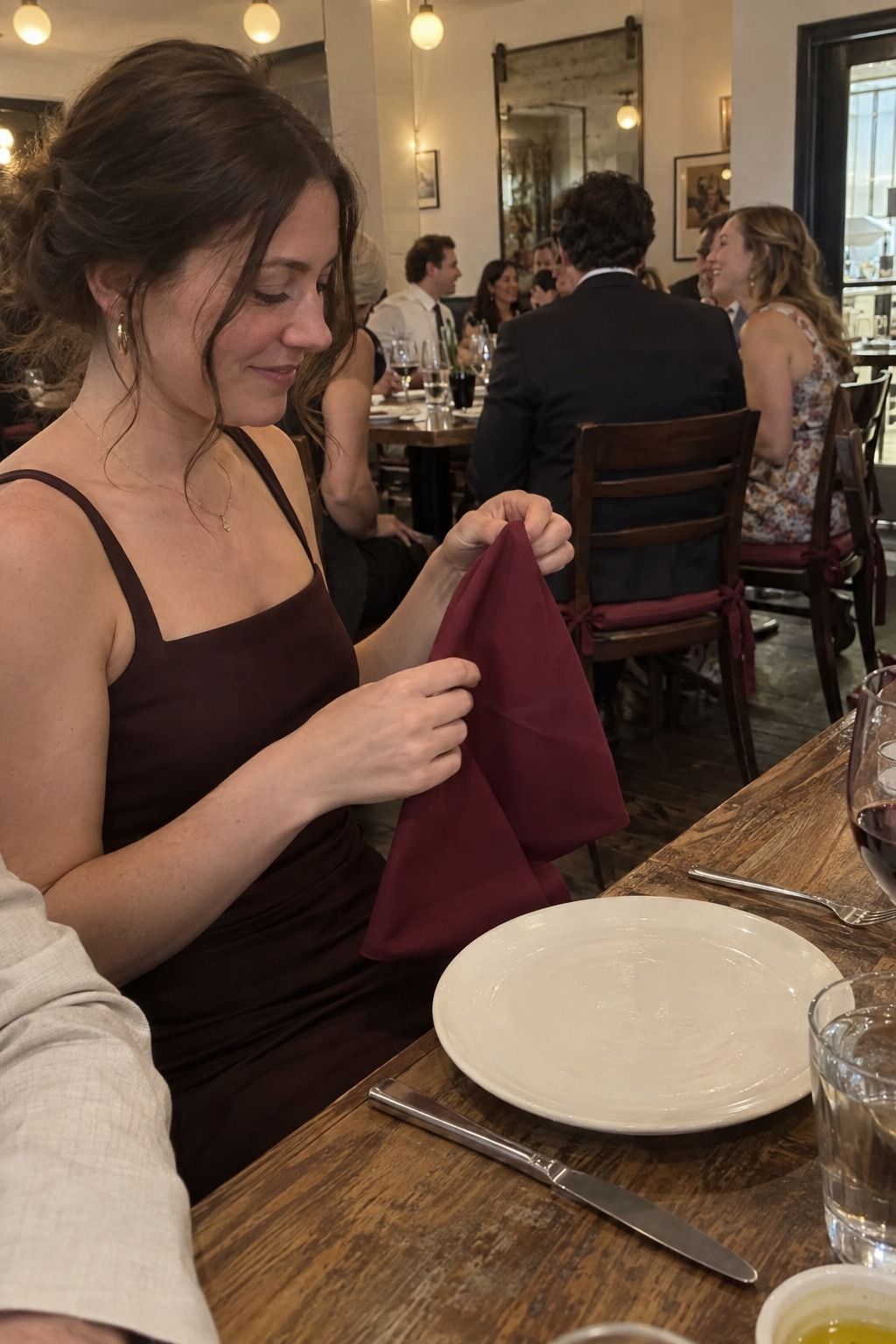 Guest unfolds a deep-garnet napkin beside an ivory plate at an intimate wedding dinner.