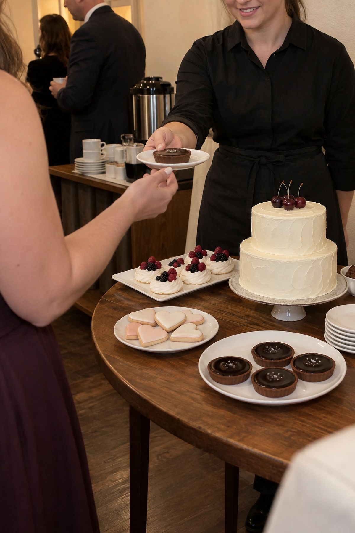A server offers a chocolate tart beside one simple romantic dessert-table focal point.