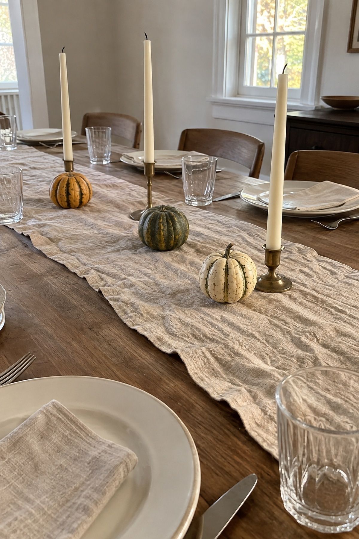 Mini gourds with visibly unlit ivory taper candles on a linen wedding table