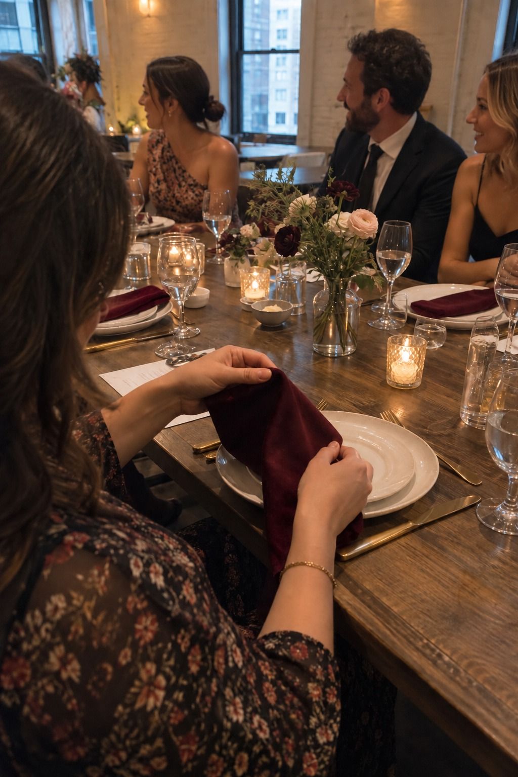 A guest handles a burgundy velvet napkin beside gold flatware at an occupied reception table.