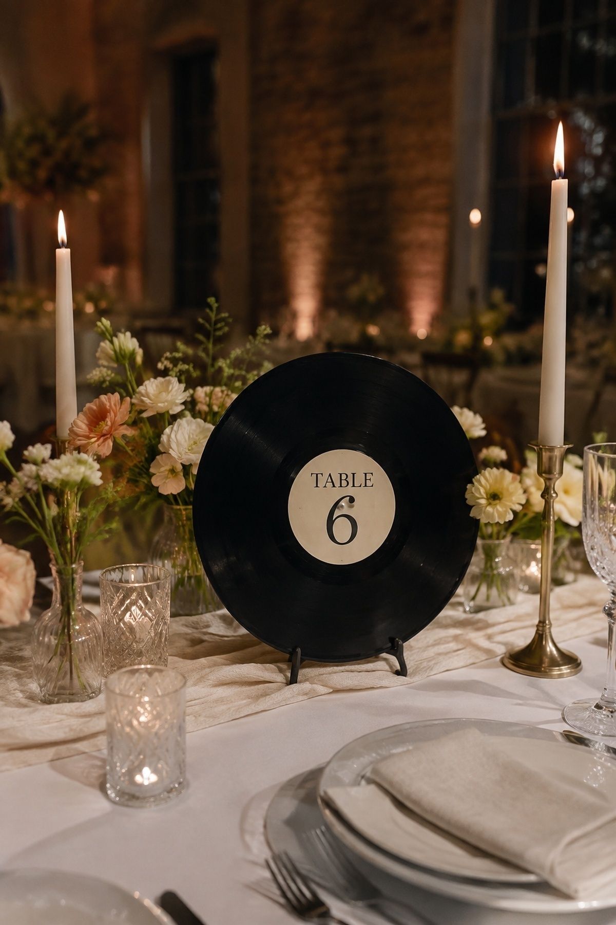 Upright vinyl record table number sign with low flowers, candles, linen, and simple place settings