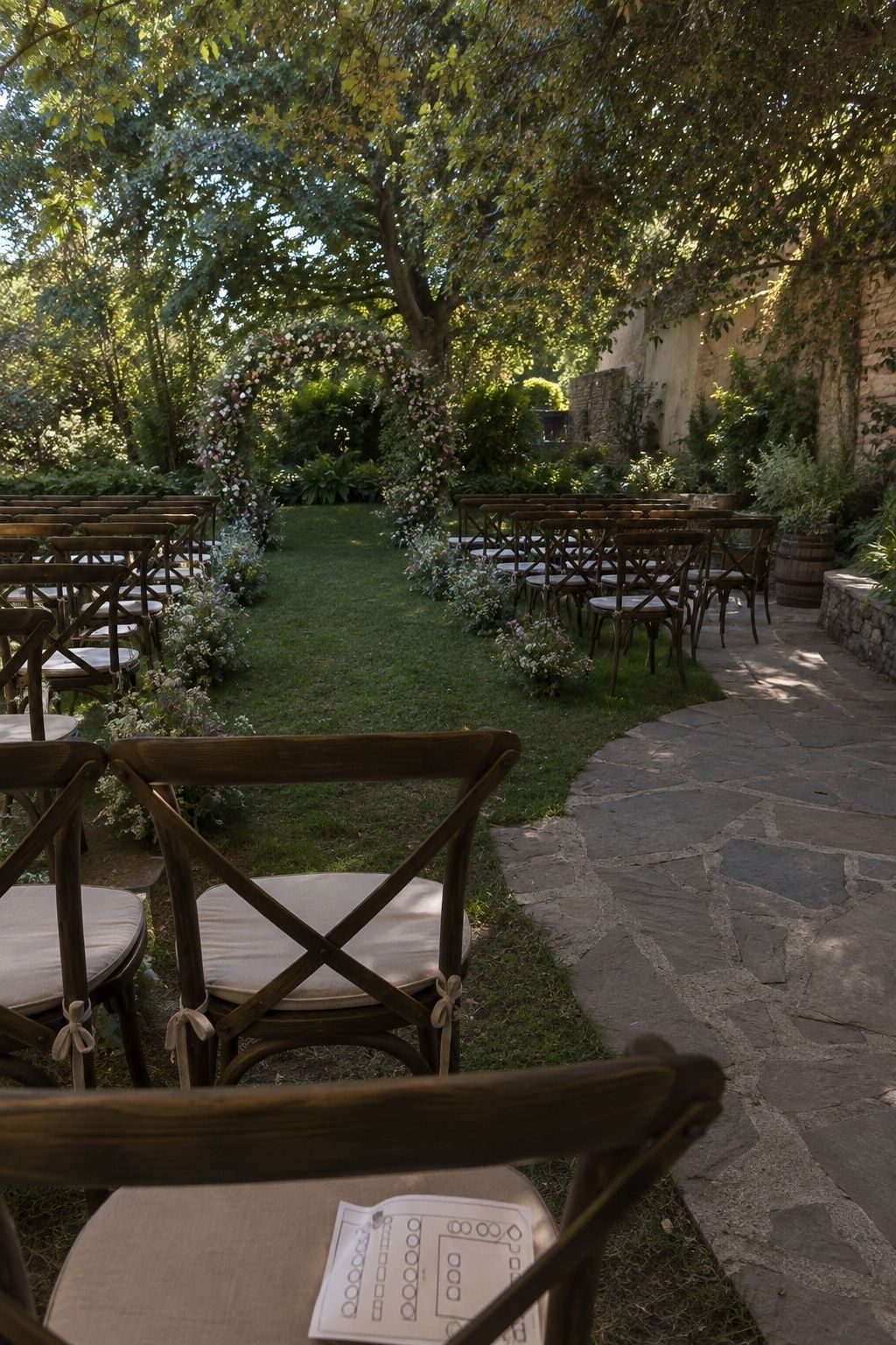 Back-row view of a shaded garden ceremony with clear arch sightlines, guest seating, wide aisle, and accessible path