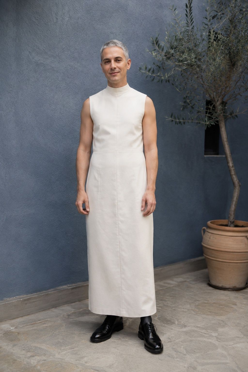 Man in a high-neck ivory dress with polished black oxford shoes.