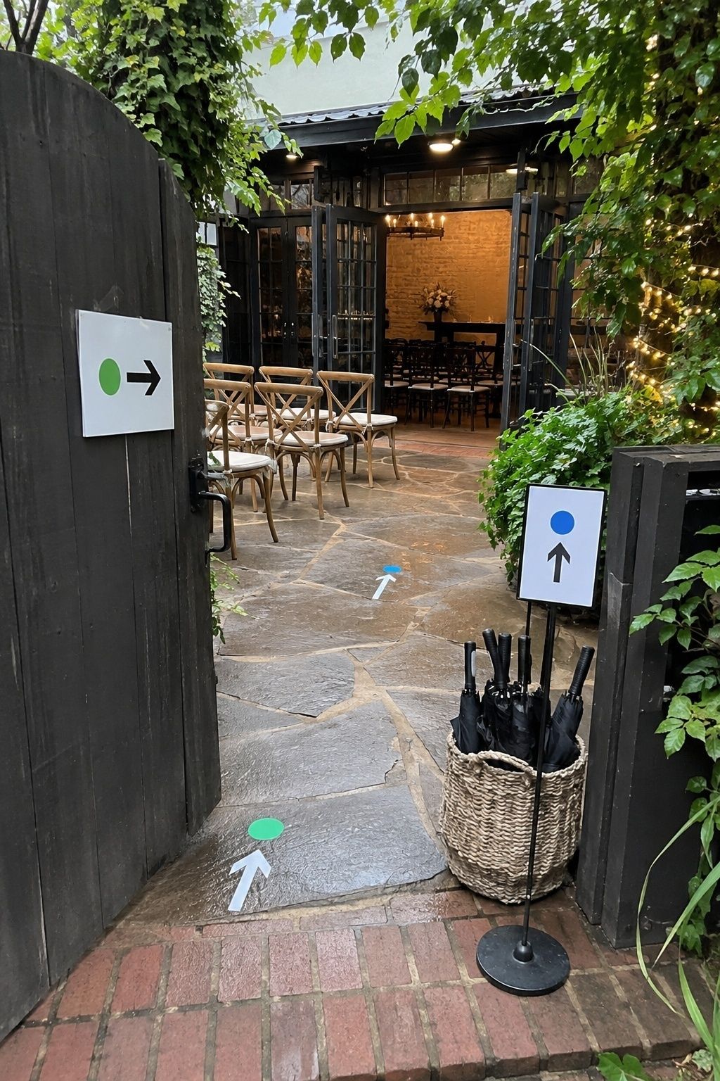 Open venue gate with arrow markers, ceremony chairs, umbrella basket, patio route, and visible indoor rain-backup room